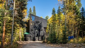 A modern two-story cabin with a garage, surrounded by a forest. - Creekside Cabin: Mountain Views, Fireplace & Sauna (Dumont)