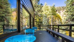A wooden deck with a table and chairs, overlooking a forested area. - Creekside Cabin: Mountain Views, Fireplace & Sauna (Dumont)