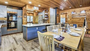 A modern kitchen with wooden cabinetry, a central island, and a dining area with wooden chairs and a table set for a meal. - Creekside Cabin: Mountain Views, Fireplace & Sauna (Dumont)
