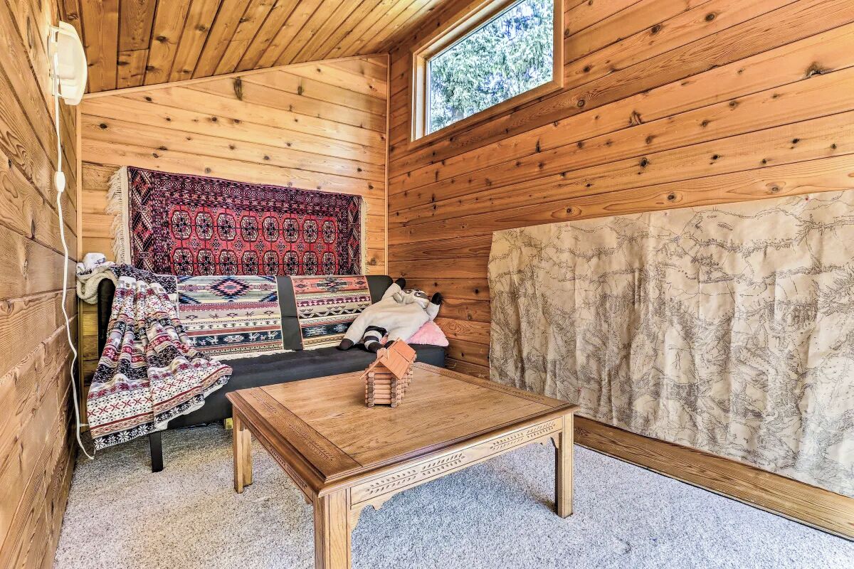 Een gezellig houten interieur met bed met opvallend beddengoed, een klein tafeltje en een raam met uitzicht op bomen.