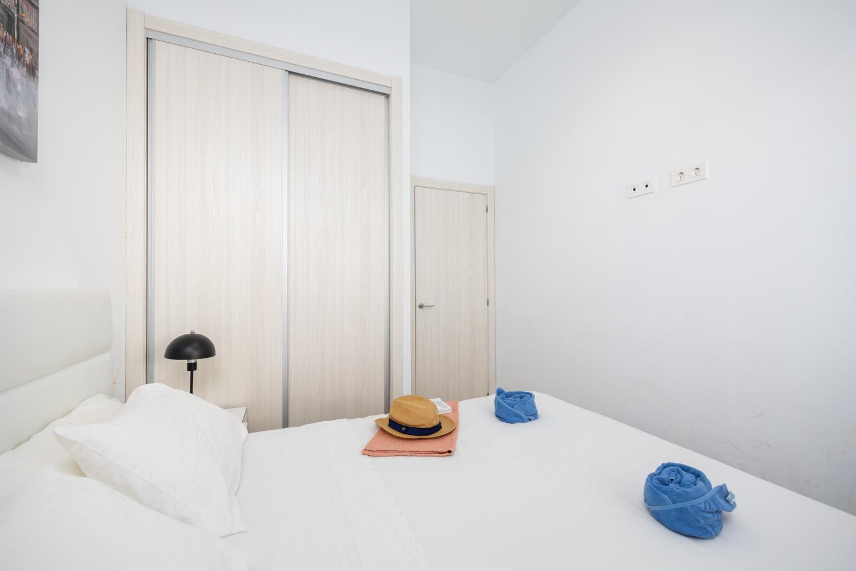 A bedroom with a bed, a wardrobe, a lamp, and a hat on the bed.