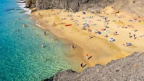 A beach with clear turquoise water, rocky cliffs, and a mountainous backdrop. - Villa Janubio With 3 Bedrooms and 2 Bathrooms (Yaiza)