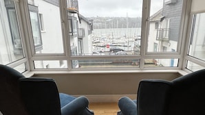 Una habitación con dos sillones azul oscuro orientados hacia un ventanal con vistas a un puerto deportivo con barcos y edificios.
