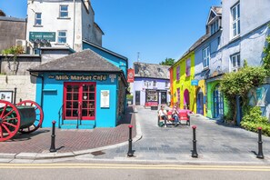 A street with colorful buildings, including a blue building with a red door labeled "The Milk Market Cafe".