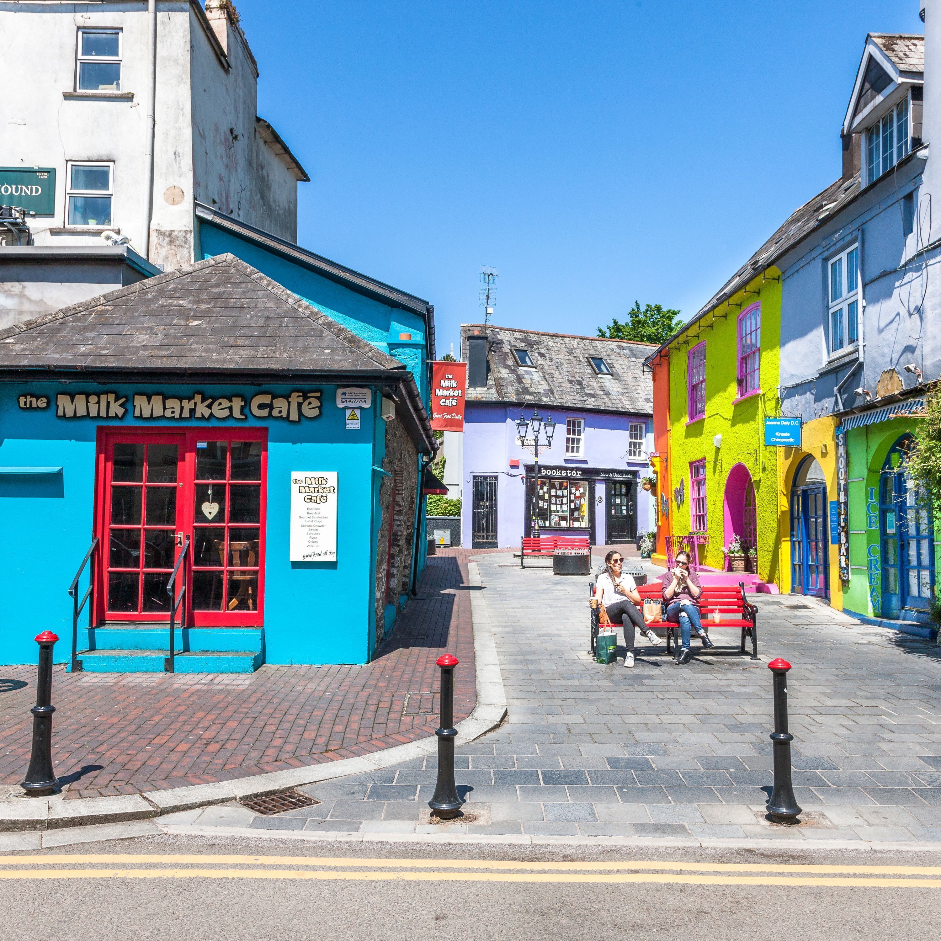 A street with colorful buildings, including a cafe named "The Milk Market Cafe".