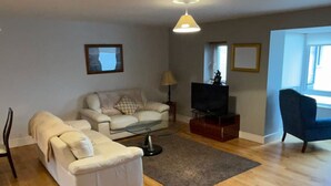 Una sala de estar con un sofá, una mesa de centro, un mueble para televisión y una silla.