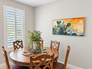 A dining area with a round wooden table, four wooden chairs, a potted plant, and a painting on the wall. - Two Heated Pools/Spas, BBQ, Golf Course (Washington)
