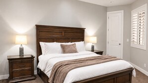 A bedroom with a large bed, two bedside tables, a door, and a window with blinds.