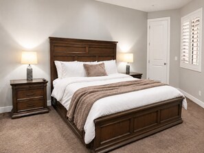 Une chambre à coucher avec un grand lit, deux tables de chevet, une porte et une fenêtre avec des stores.