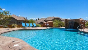 A clear swimming pool with blue water, surrounded by lounge chairs and a small waterfall feature.