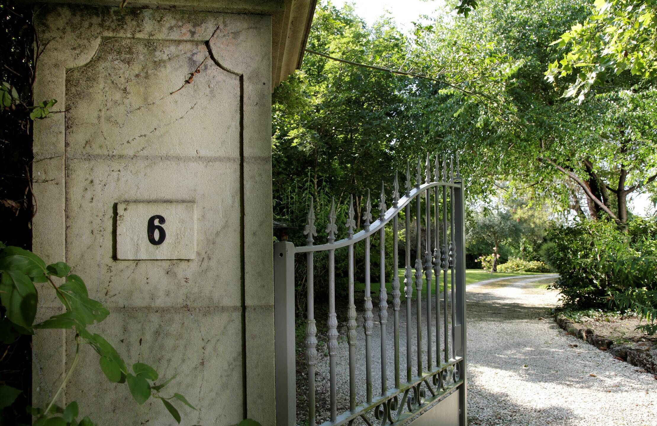 Een poort met een nummer '6' bord, omgeven door weelderige begroeiing en een grindpad.
