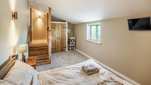 A bedroom with a bed, a TV, a window, and a staircase leading to another room. - The Old Stables 2 - UK46683 (Shipton-Under-Wychwood)