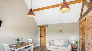 A dining area with a wooden table and chairs, a sofa, and a hanging light fixture. - The Old Stables 2 - UK46683 (Shipton-Under-Wychwood)