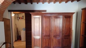 Un'ampia stanza con un armadio in legno, pavimento piastrellato e un arco in mattoni che conduce a un'altra stanza.
