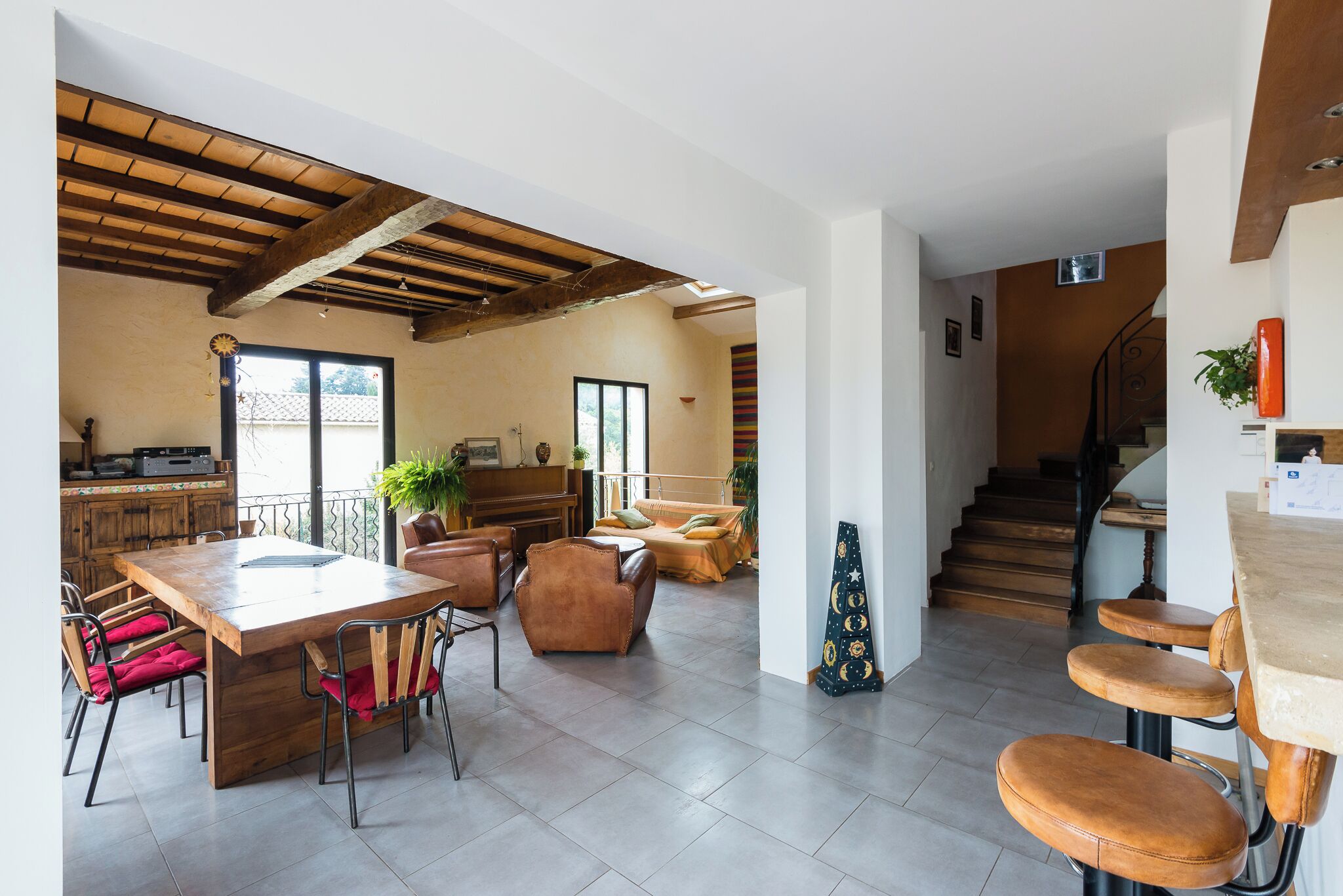 A spacious living area with a wooden dining table, comfortable seating, a staircase, and a kitchen area.