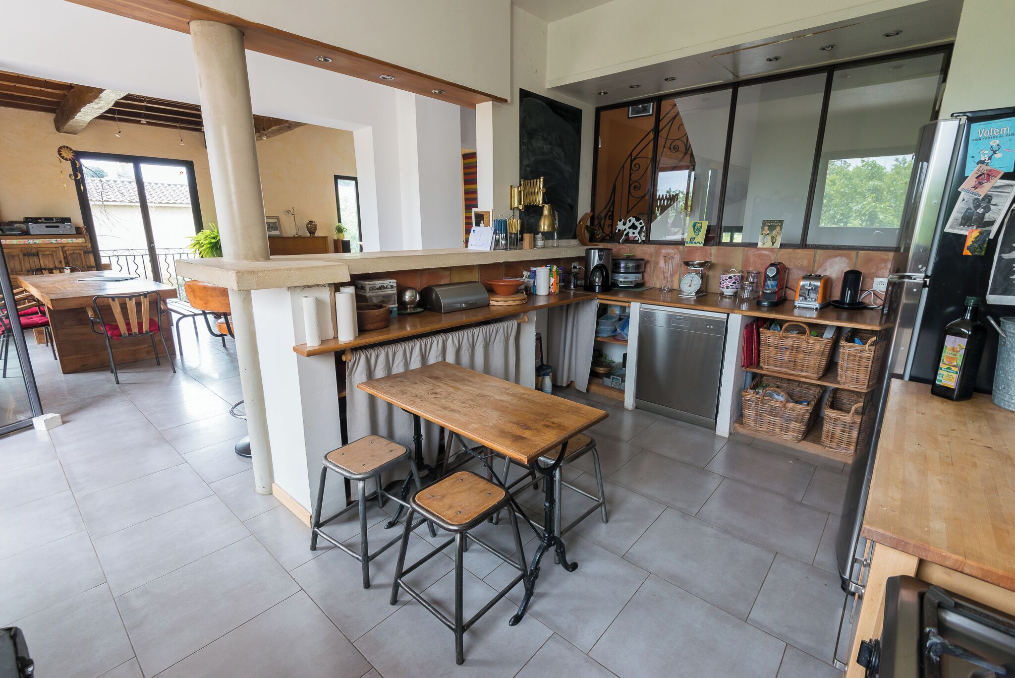 A modern kitchen with a wooden table and stools, a built-in oven, and various appliances.
