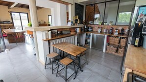 A modern kitchen with a wooden table and stools, a built-in oven, and various appliances. - Location Grande Villa au Soleil D'avignon (Châteauneuf-de-Gadagne)