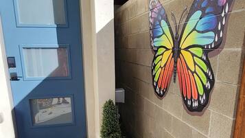 A building entrance with a blue door, a small potted plant, and a colorful butterfly mural on the wall.
