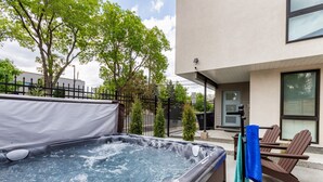 Un bain à remous avec une tablette, une chaise et un porte-serviettes, installé à l’extérieur, avec un bâtiment en arrière-plan.