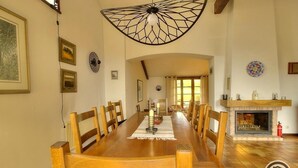A dining room with a long wooden table, chairs, a chandelier, framed pictures, a fireplace, and a tiled floor. - La Ponie - Cenves - Gîte (CENVES)