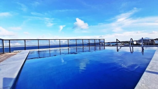 Una piscina con vista despejada al océano, barandilla de vidrio y terraza de madera.
