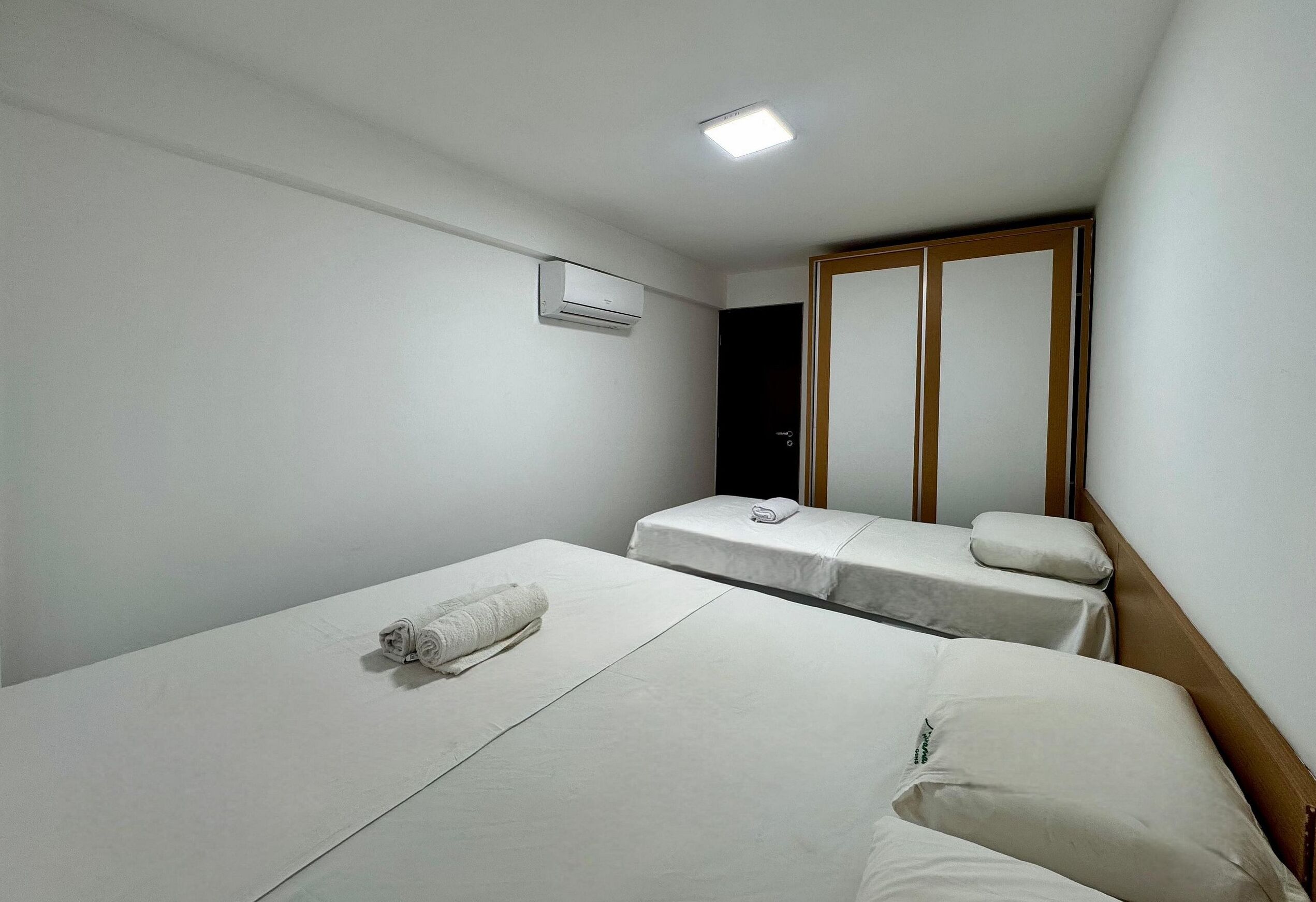 A hotel room with two single beds, a wooden wardrobe, a mirror, and an air conditioning unit.