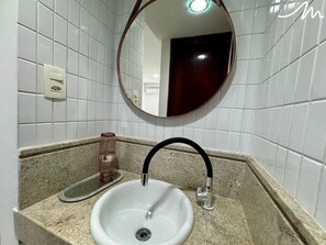 Casa de banho com lavatório branco, espelho e dispensador de toalhas.
