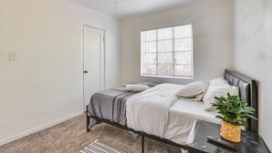 A bedroom with a bed, a bedside table with a plant, a window with blinds, and a ceiling light. - Pet-friendly Condo < 1 Mi to Phoenix College! (Phoenix)