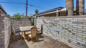 A patio area with a brick wall, a wooden table, and two chairs. - Pet-friendly Condo < 1 Mi to Phoenix College! (Phoenix)