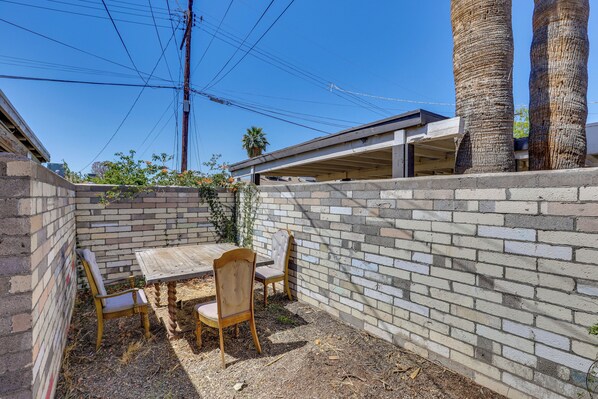 A patio area with a brick wall, a wooden table, and two chairs.