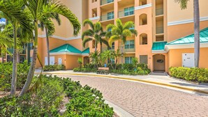 A hotel courtyard with palm trees, a paved walkway, and a building with balconies and a green awning. - Bayfront Punta Gorda Condo Rental w/ Pool Access! (Punta Gorda)