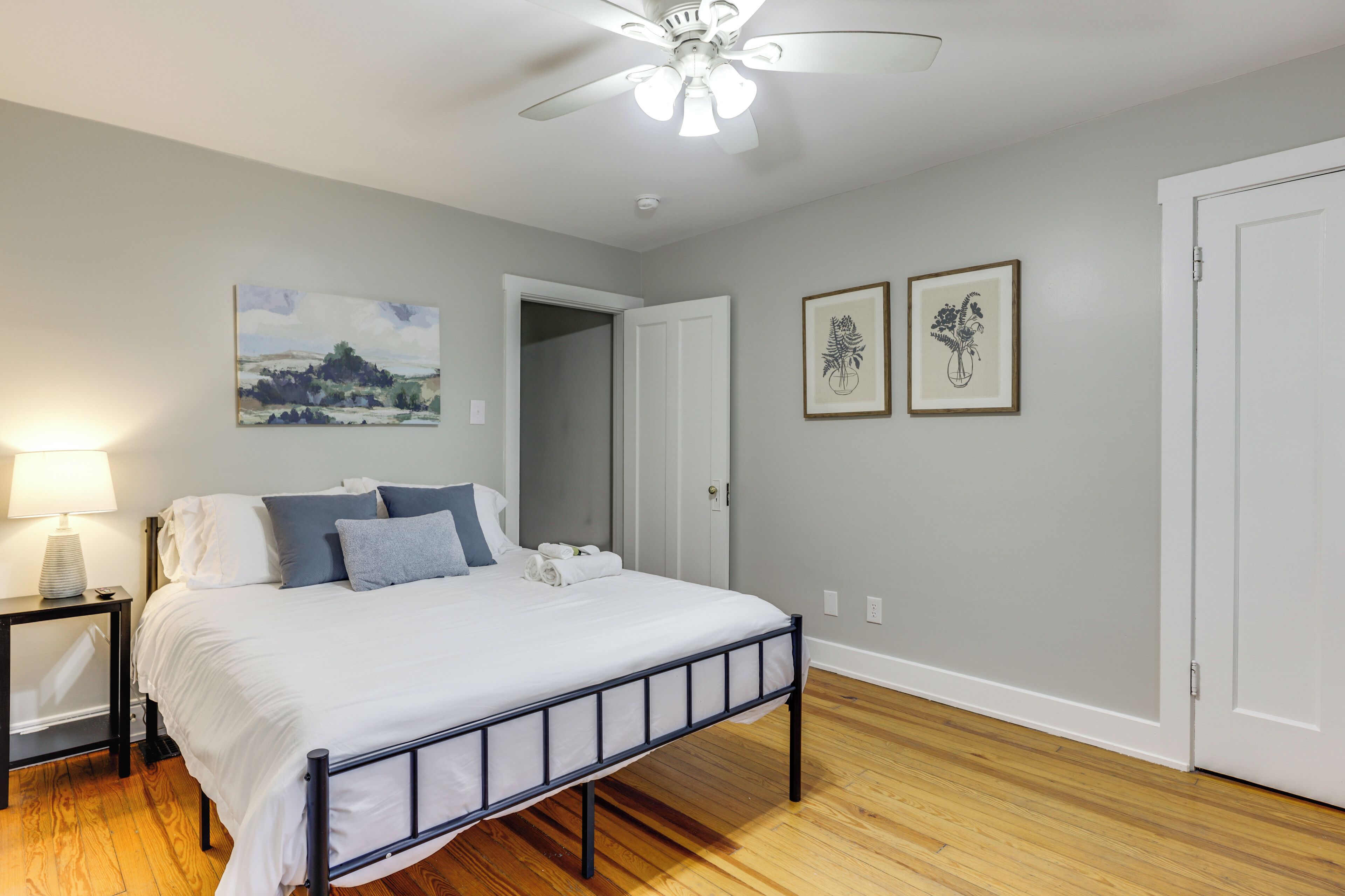 A bedroom with a bed, a nightstand, a ceiling fan, and two framed pictures on the wall.