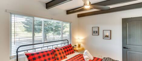 A bedroom with a bed, a ceiling fan, a window with blinds, a bedside table with a lamp, and a door.