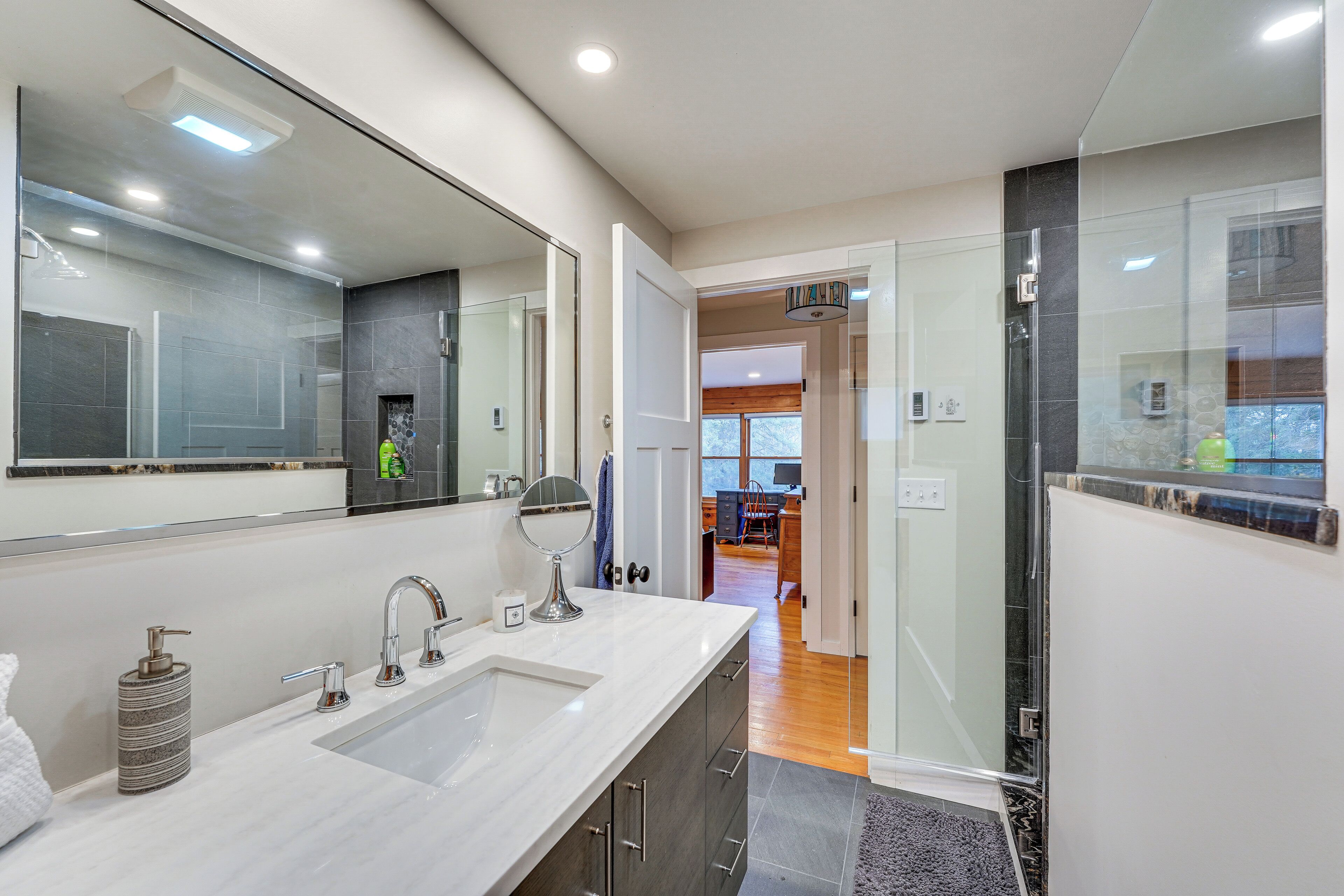 A modern bathroom with a large mirror, dual sinks, and a shower area.