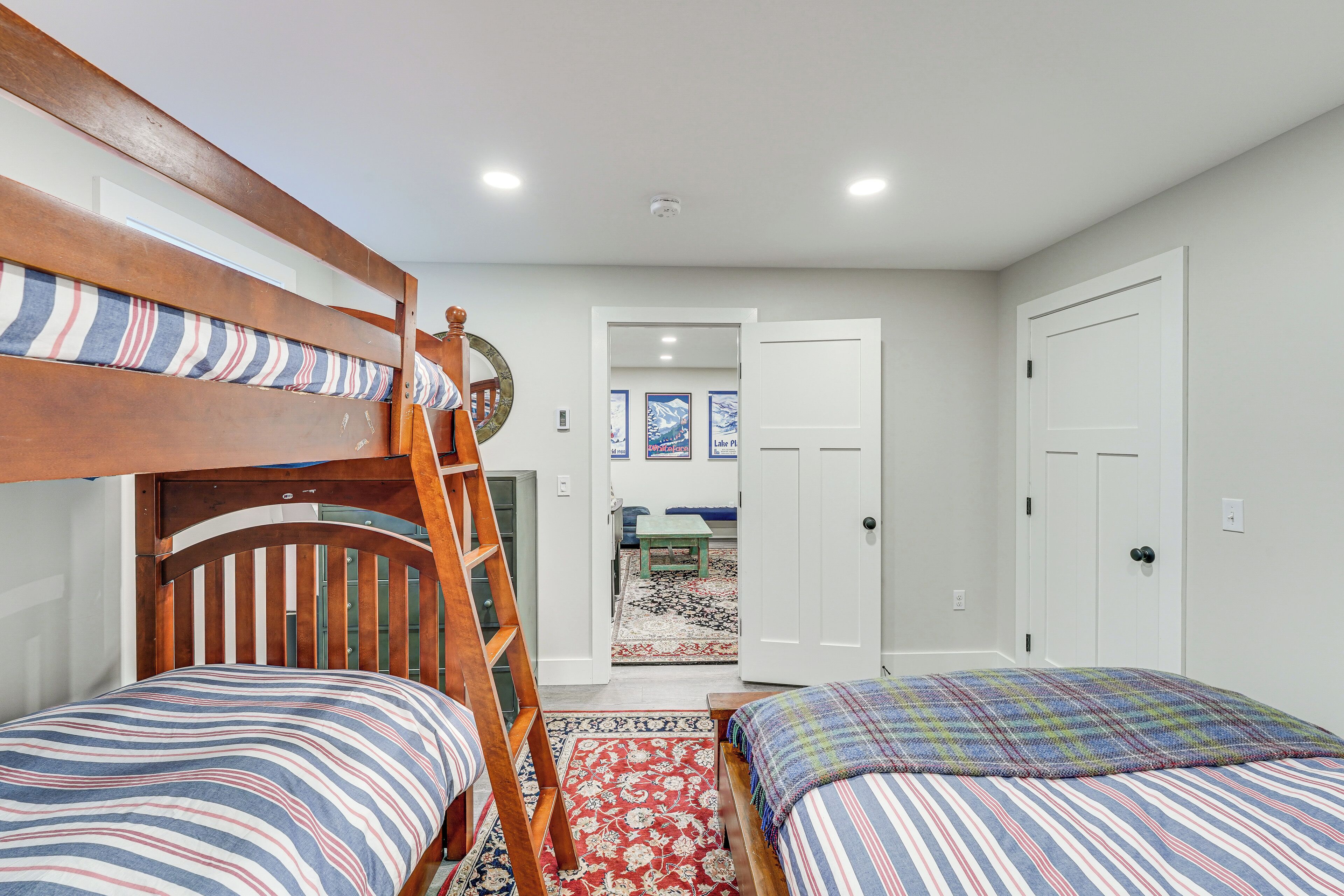 Un dormitorio con literas, una escalera de madera, un tapete floral rojo y una puerta que da a otra habitación.