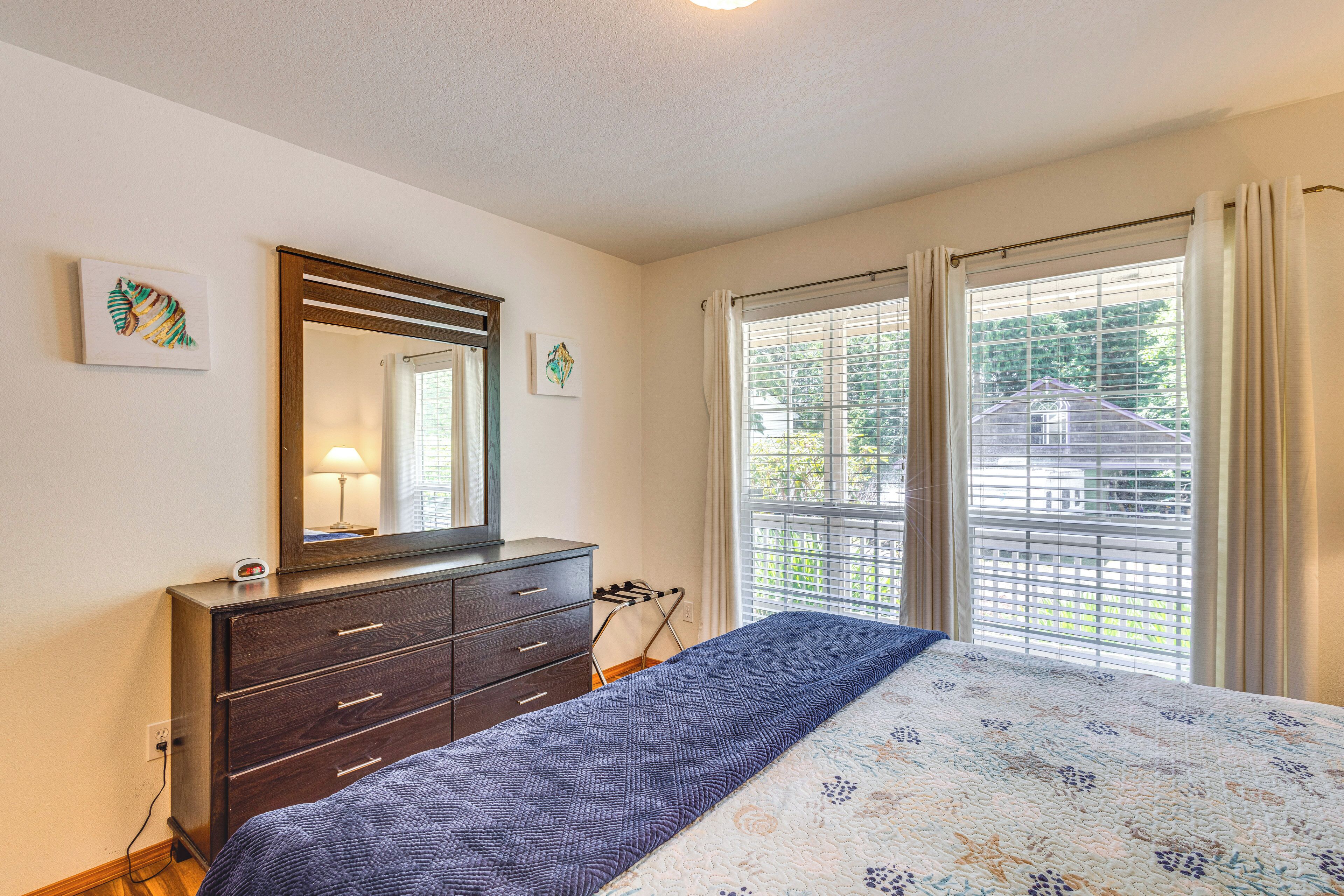 A bedroom with a bed, dresser, mirror, and windows with blinds.