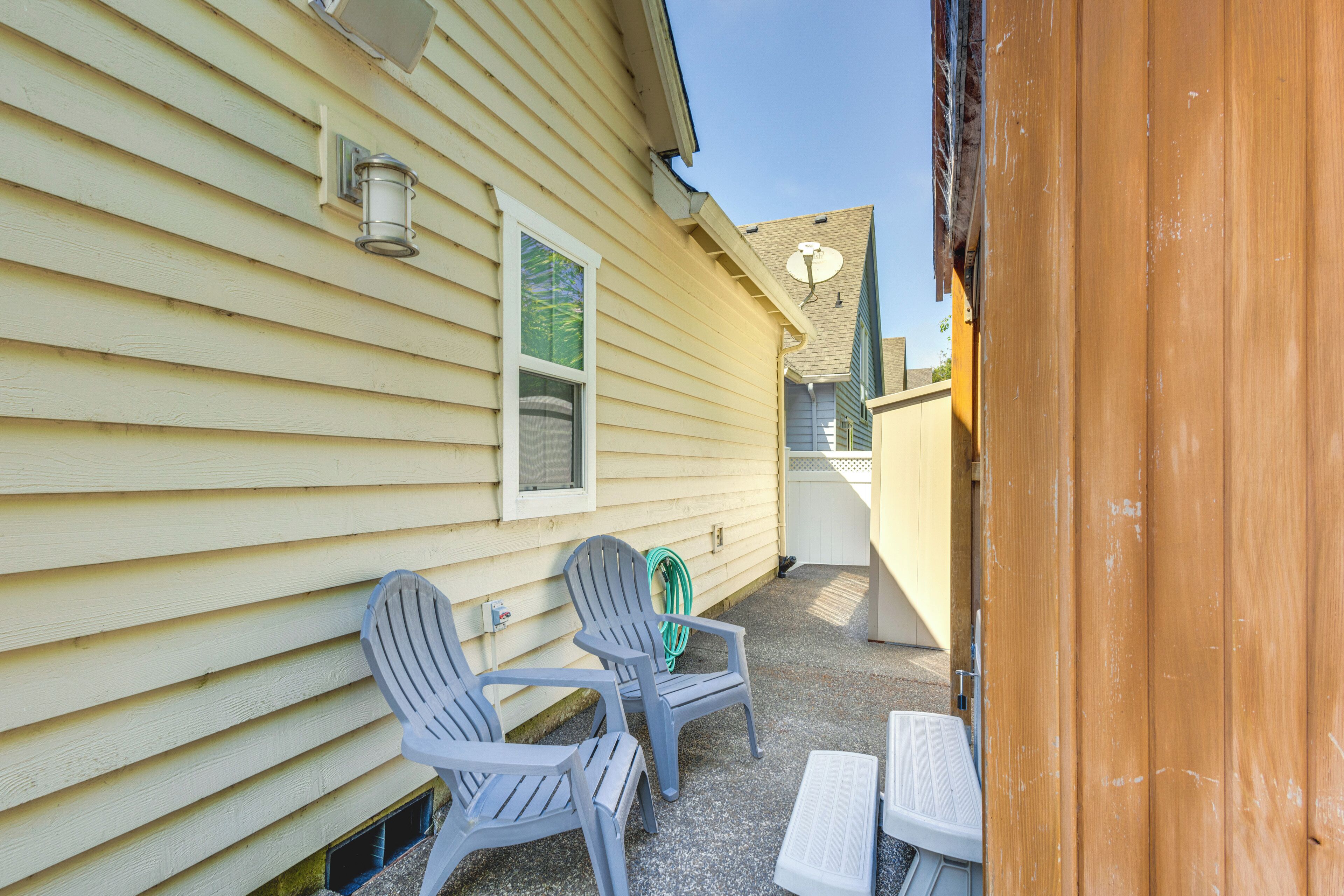 A covered patio with two Adirondack chairs and a small table, adjacent to a house with yellow siding and a window.