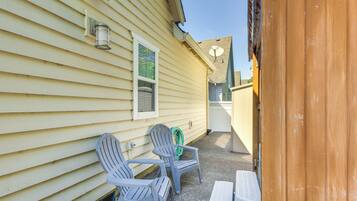A covered patio with two Adirondack chairs and a small table, adjacent to a house with yellow siding and a window.