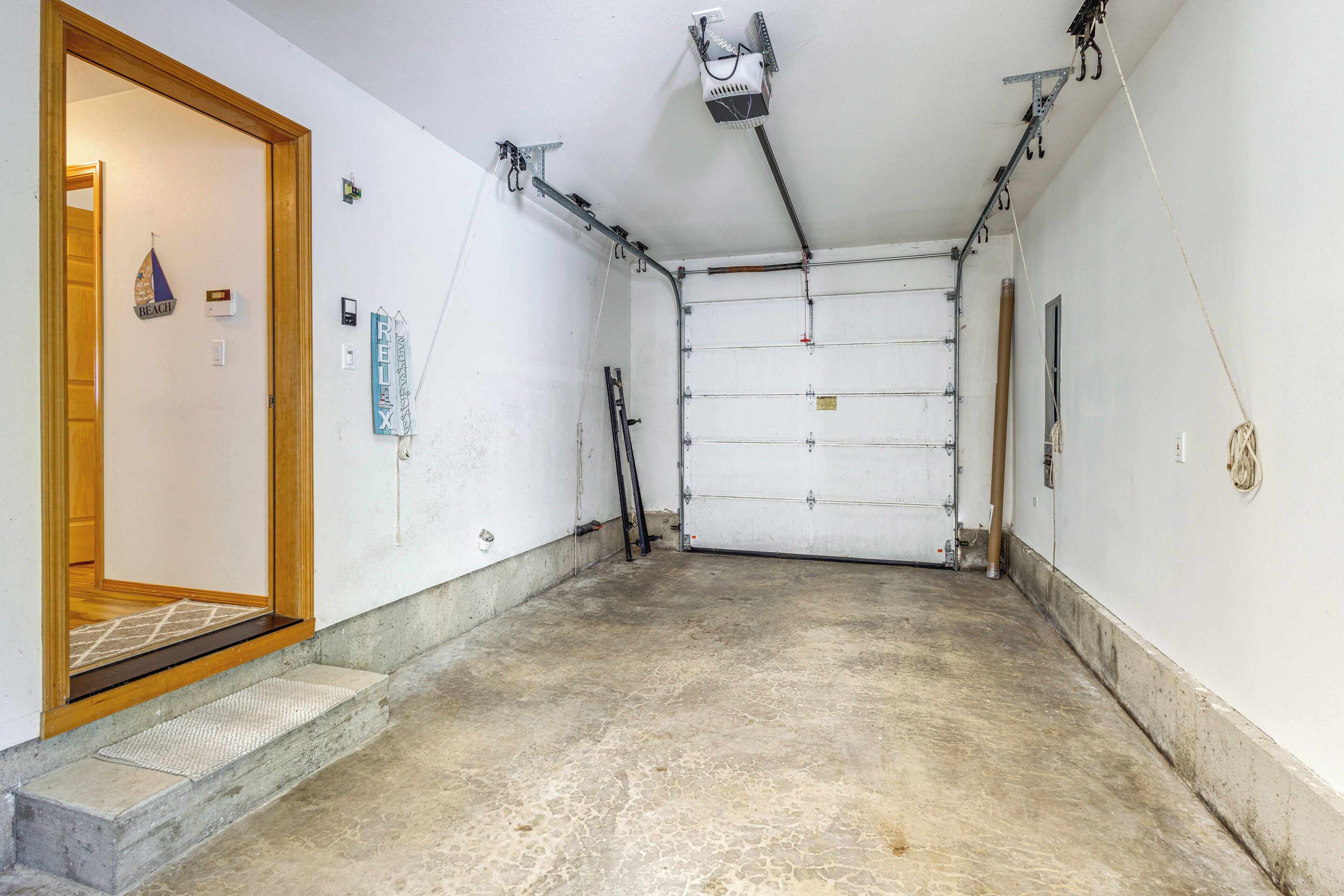 A garage with a concrete floor, a wooden door, and a ceiling with exposed pipes and a fan.