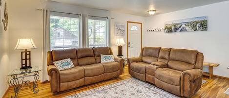 A living room with two brown leather sofas, a glass coffee table, a patterned rug, and a wooden floor.