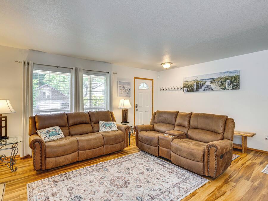 A living room with two brown leather sofas, a glass coffee table, a patterned rug, and a wooden floor.