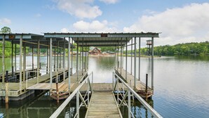 A wooden pier leading to a covered dock area with a view of a house across the water. - Waterfront Lake Hamilton Vacation Rental w/ Dock! (Royal)