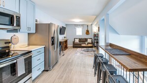 A modern kitchen with stainless steel appliances, a dining area with a wooden table, and a living space with a sofa and a guitar. - Waterfront Lake Hamilton Vacation Rental w/ Dock! (Royal)