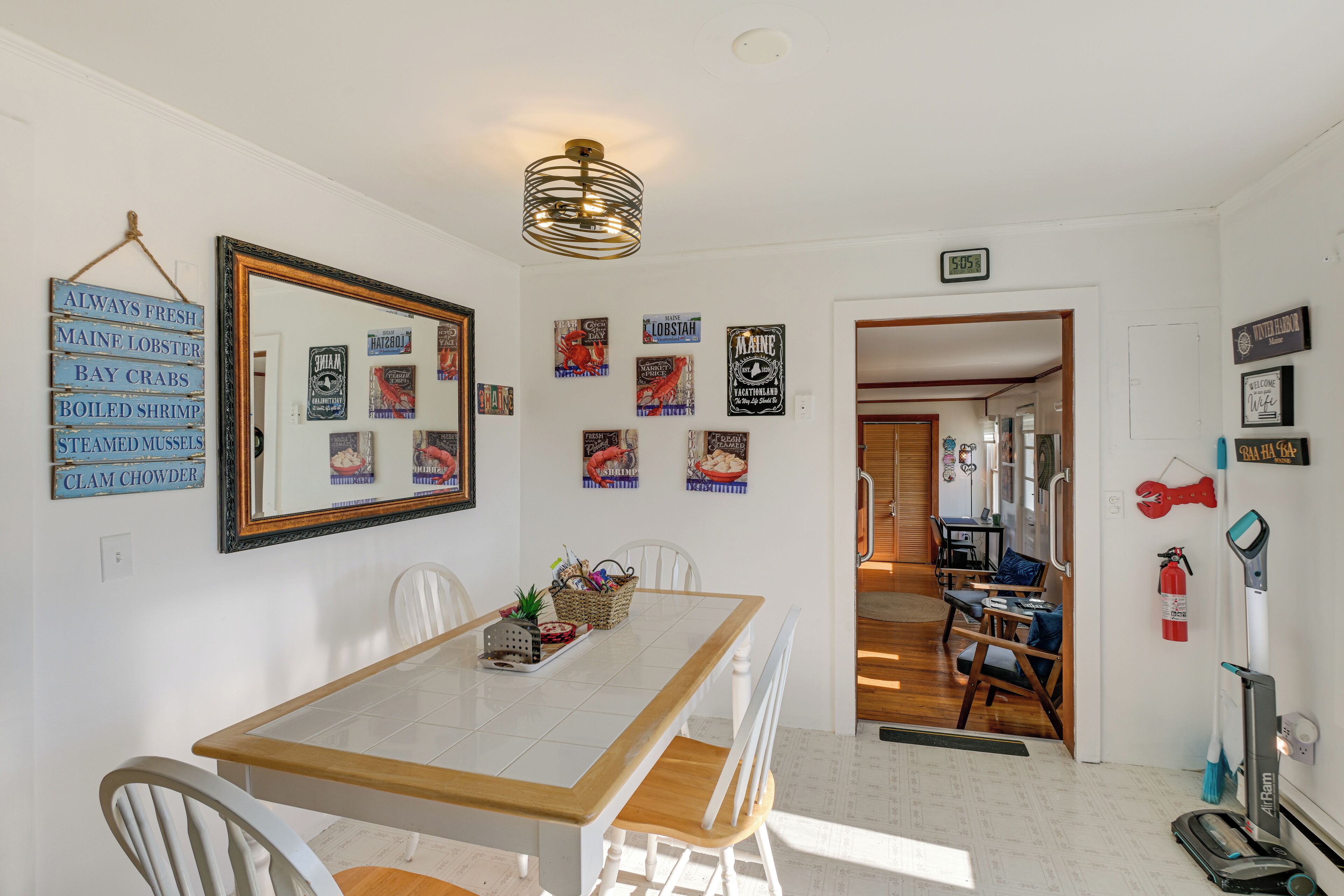 A dining area with a wooden table and chairs, a hanging mirror, and various wall decorations including signs and framed pictures.
