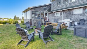 Een terras buiten met Adirondack-stoelen, een houten tafel en een barbecueplaats.