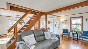 Een ruime woonkamer met een houten trap, een grijze leren bank en een eethoek met houten stoelen.