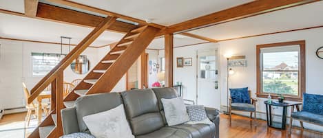 A spacious living area with a wooden staircase, a grey leather sofa, and a dining area with wooden chairs.