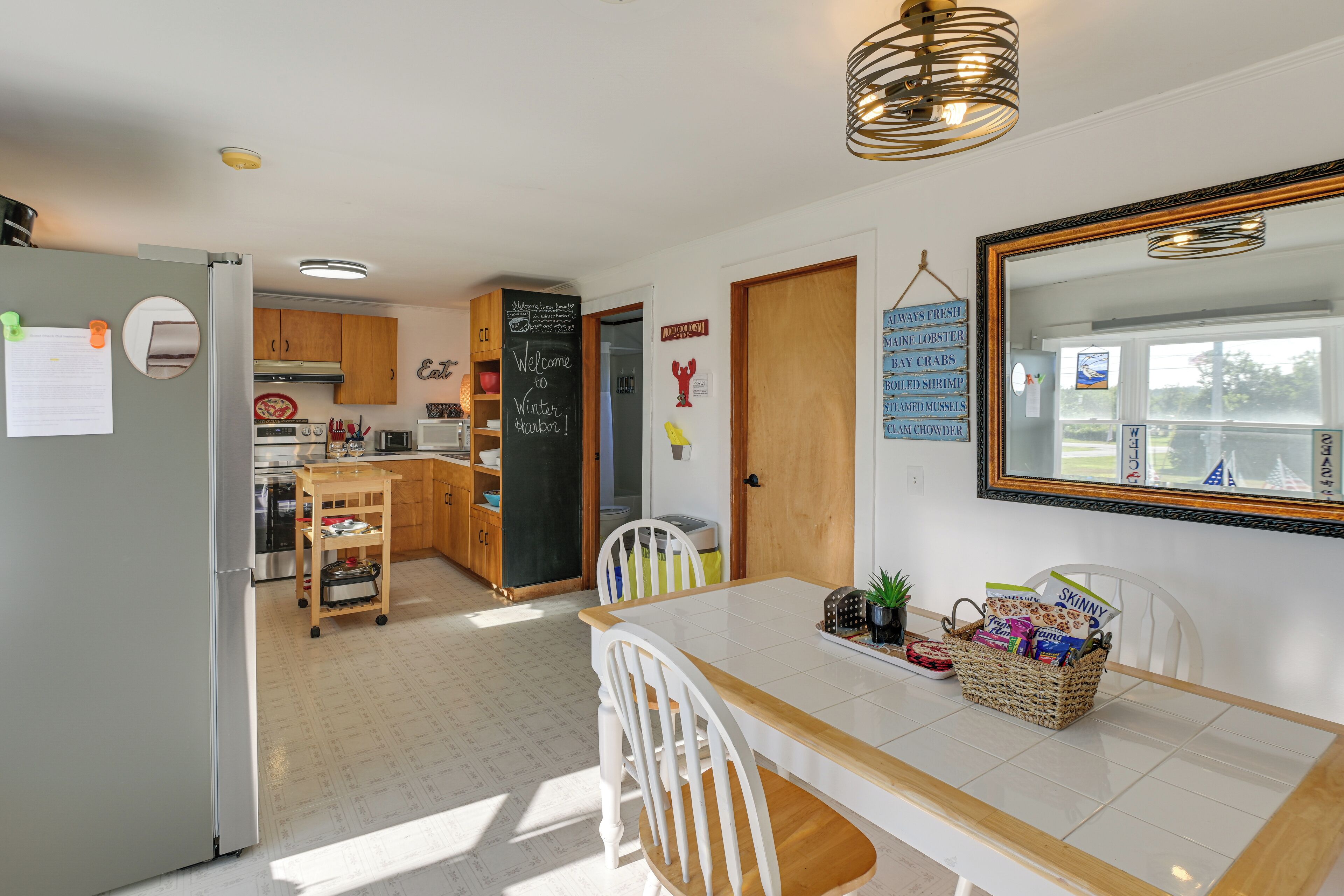 A kitchen with a refrigerator, wooden cabinets, a chalkboard, and a dining table with chairs.