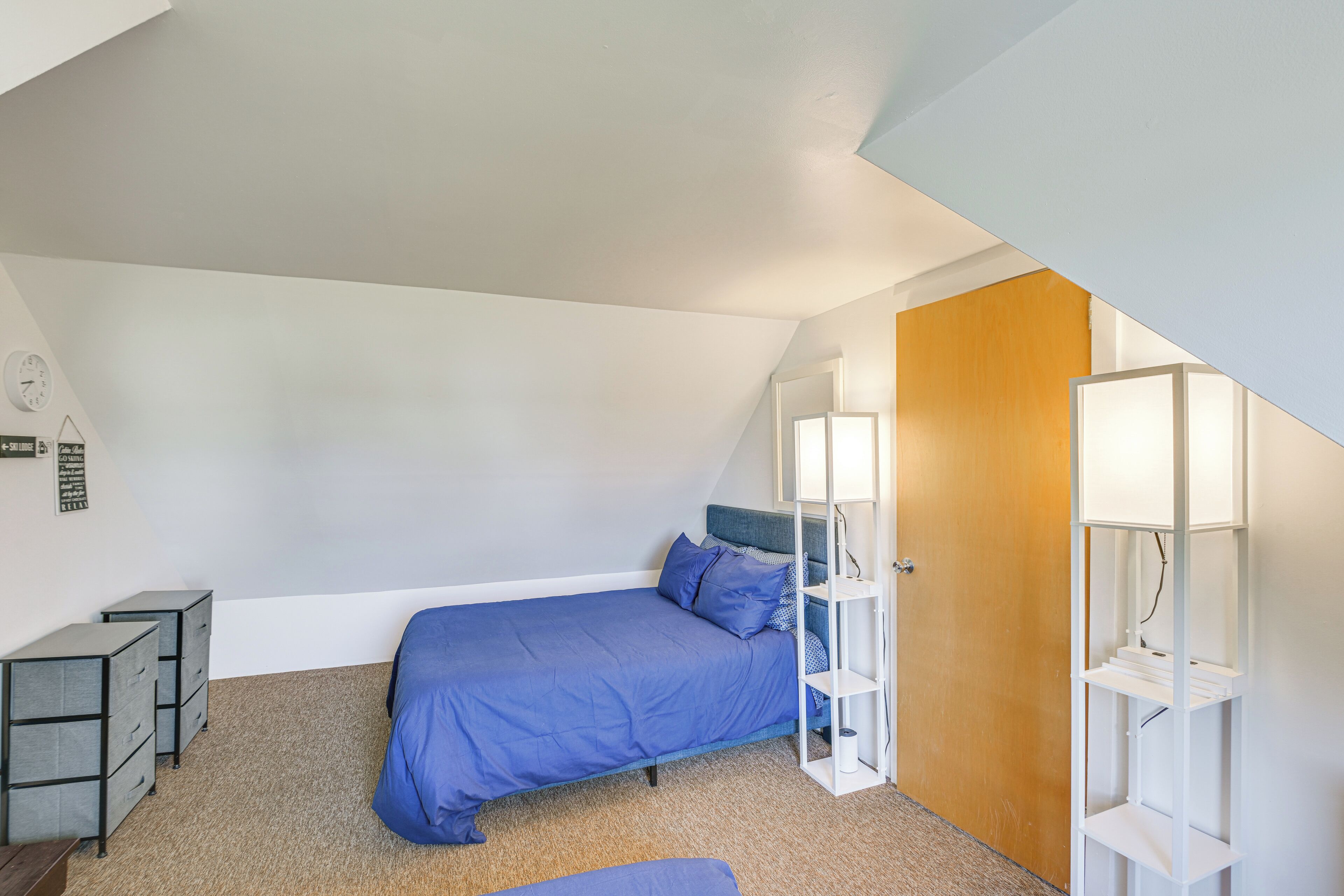 A bedroom with a single bed, a nightstand, a dresser, and a shelving unit against the wall.
