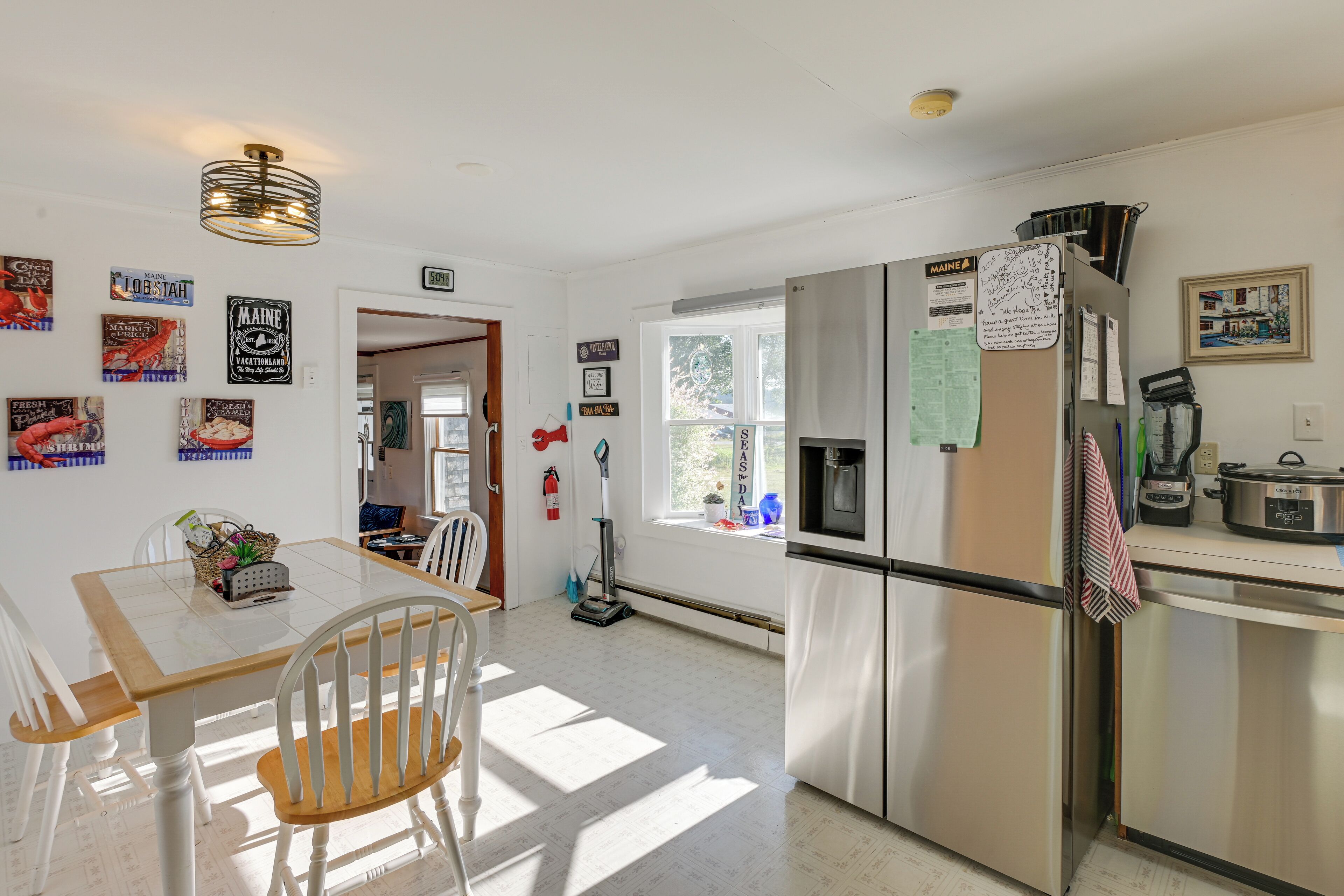 A kitchen with a stainless steel refrigerator, a dining table with chairs, and various wall decorations including signs and a framed picture.